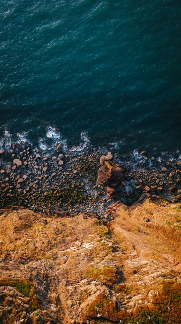 A Stunning Aerial View Of A Rocky Cliff Meeting The Ocean, Highlighting Nature's Beauty.