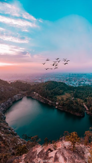 Stunning Aerial Photo Capturing Birds Flying Over A Lake With Cityscape And Sunrise In The Background. wallpaper preview