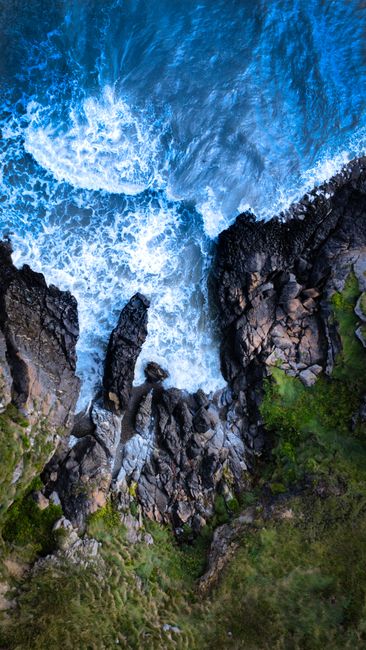 A Breathtaking Aerial View Of Waves Crashing Against Rugged Cliffs And Rocks, Showcasing Nature's Raw Power. wallpaper preview