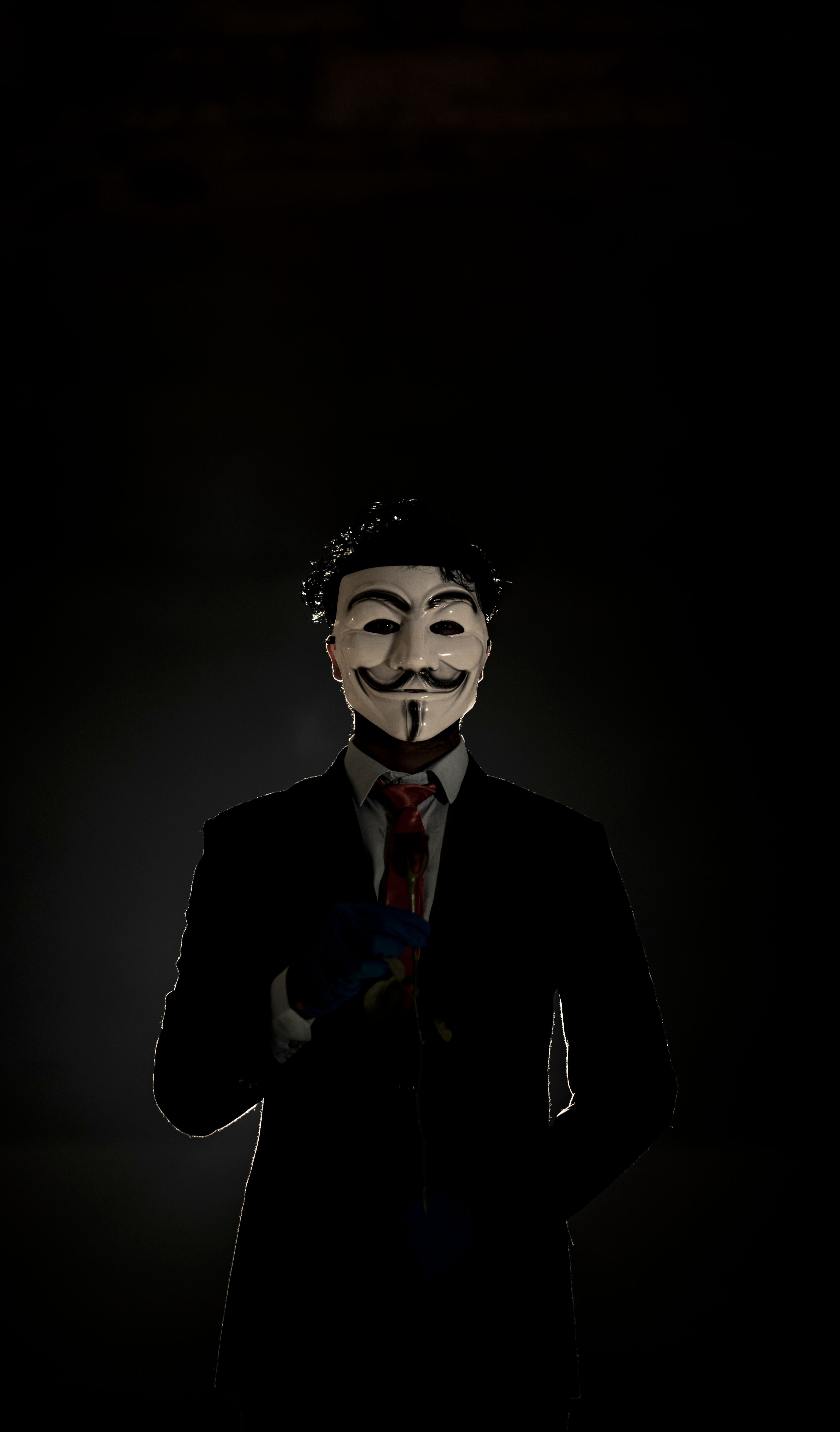Mysterious Figure In A Suit Wearing An Anonymous Mask In A Shadowy Environment. HD mobile wallpaper