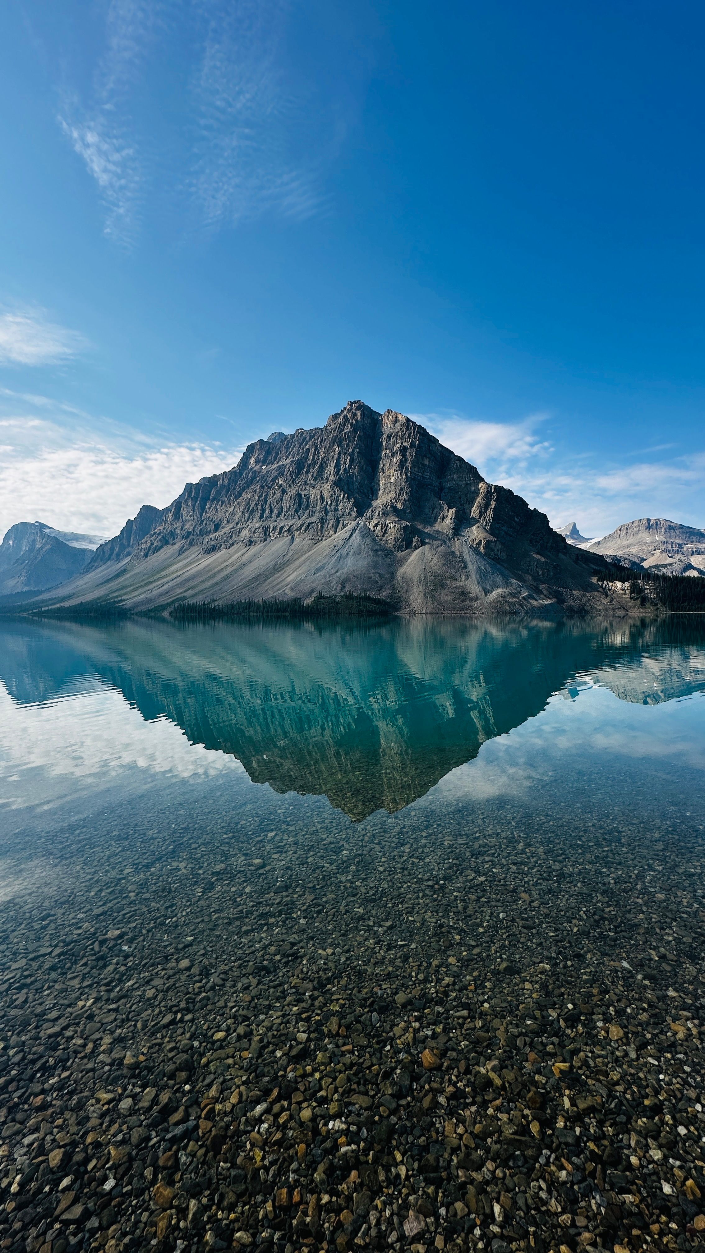 A Breathtaking Mountain View Reflected In A Clear, Tranquil Lake Under A Bright Blue Sky. HD mobile wallpaper