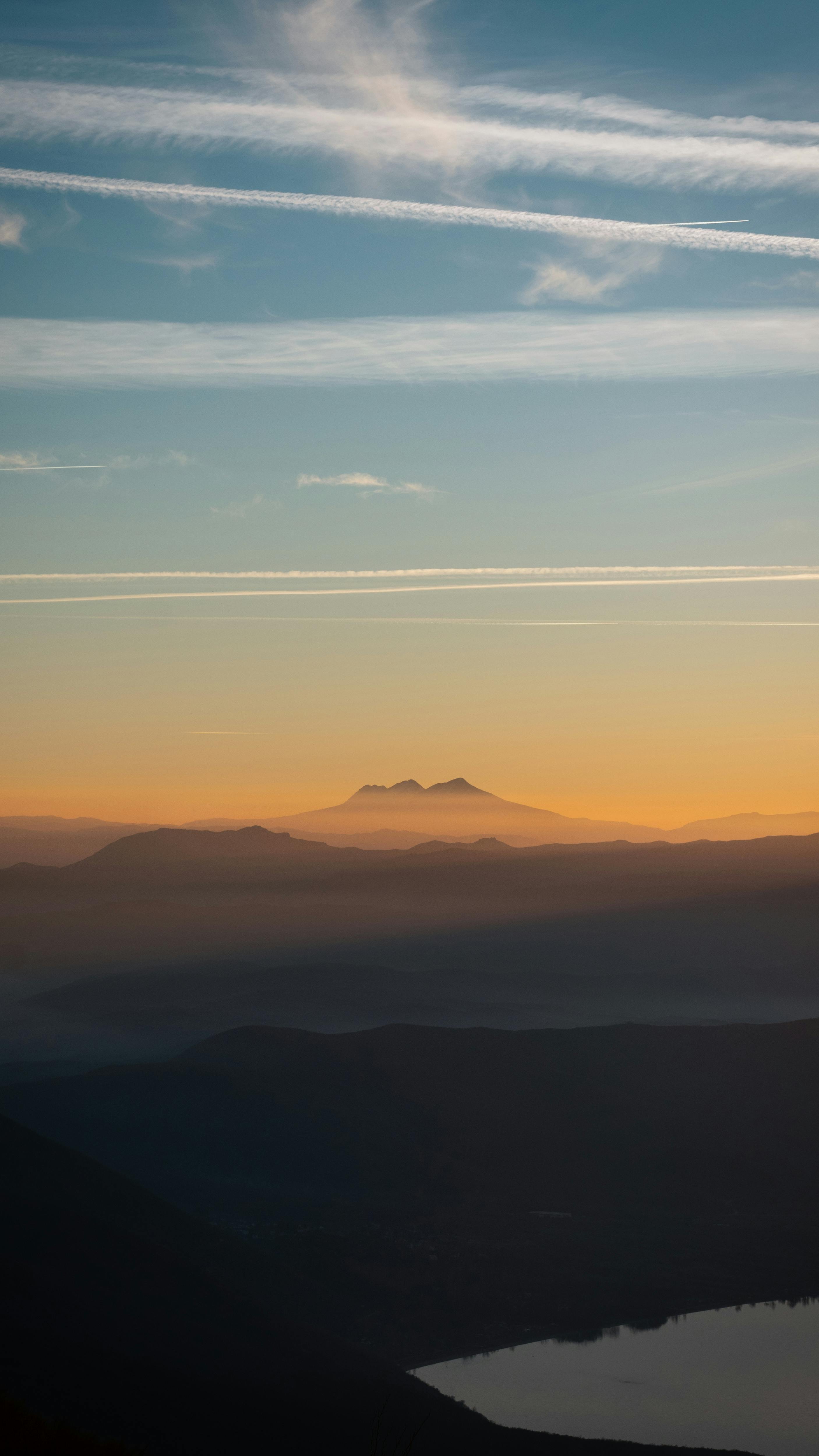 A Tranquil Sunset Scene Over Mountain Ranges With A Clear Sky And Contrails. HD mobile wallpaper