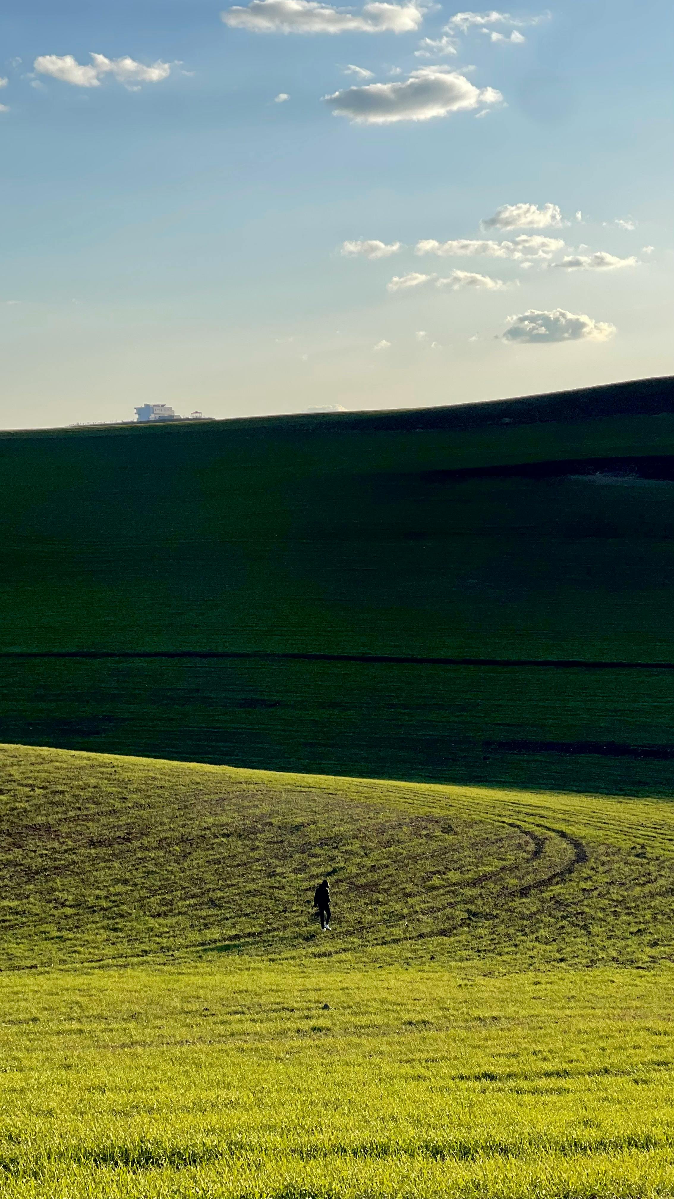 A Solitary Figure Walks Through Lush Green Hills Under A Clear Blue Sky. HD mobile wallpaper