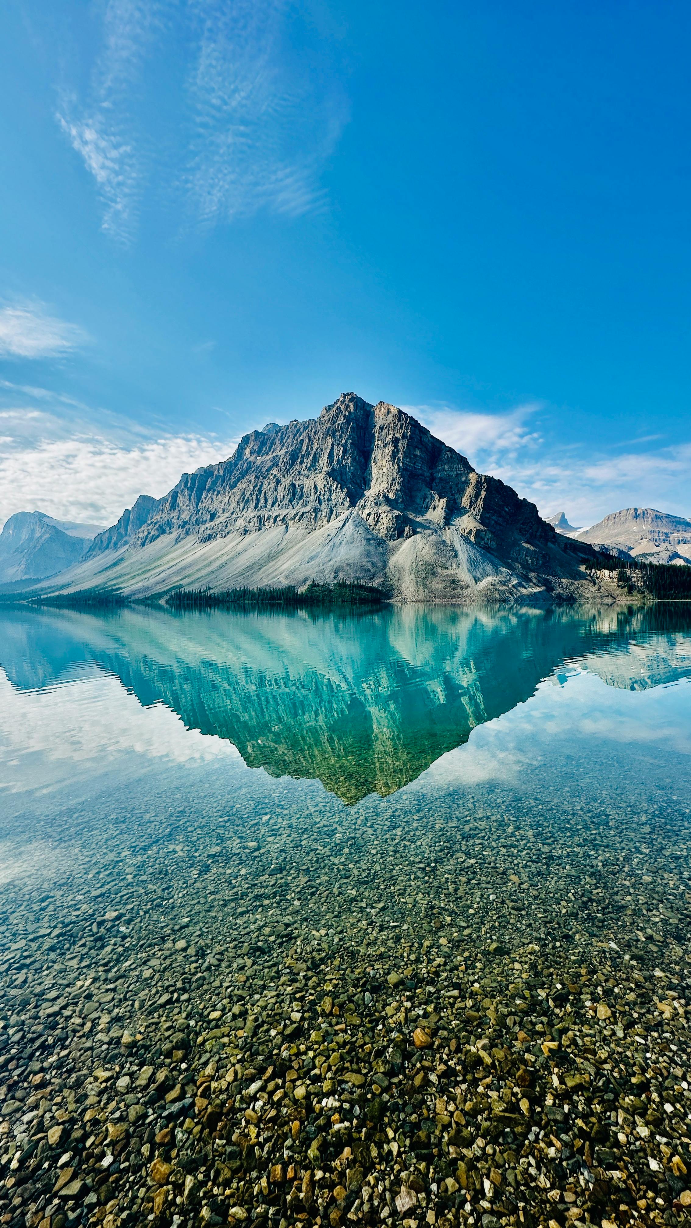 Majestic Mountain Reflected In Clear Blue Lake Under A Bright Sky, Offering A Serene Nature View. HD mobile wallpaper