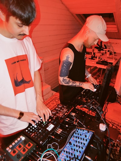 Two Men Operating Electronic Music Equipment Under Red Light. wallpaper preview