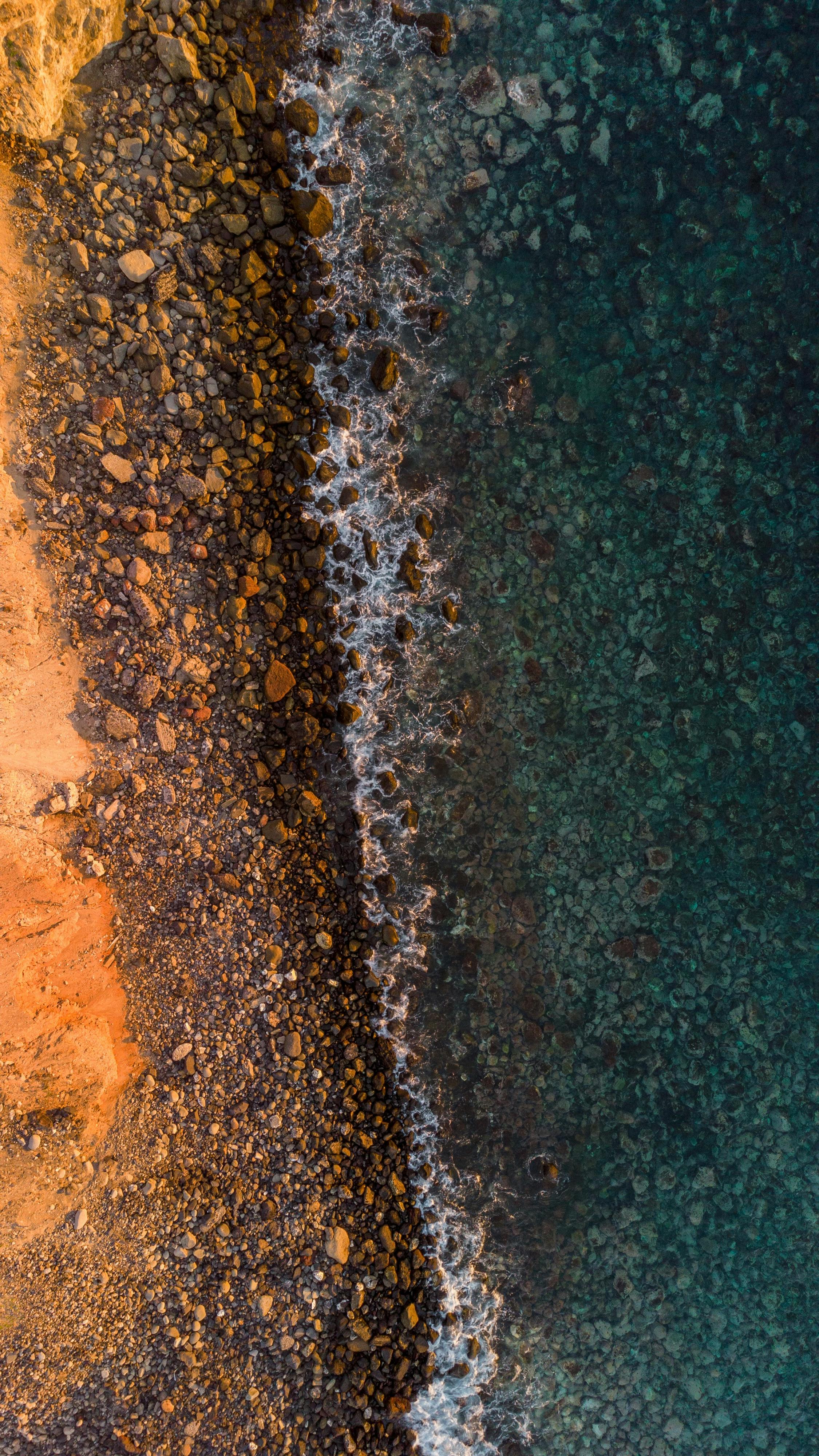 Aerial Shot Capturing The Vibrant Contrast Of A Rocky Coastline Meeting Clear Ocean Waters. HD mobile wallpaper