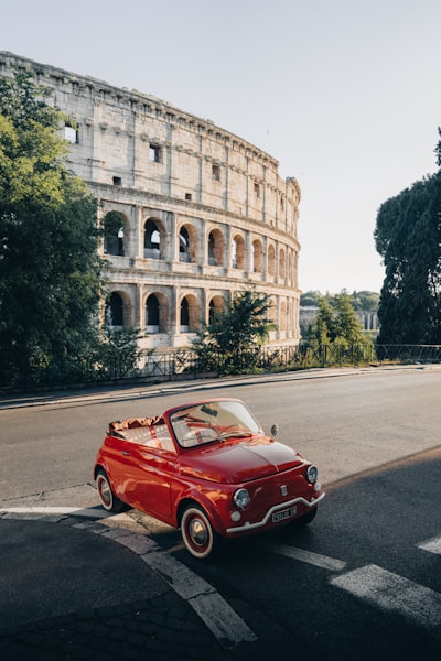 A Red Vintage Car Parked Near The Ancient Roman Colosseum. wallpaper preview