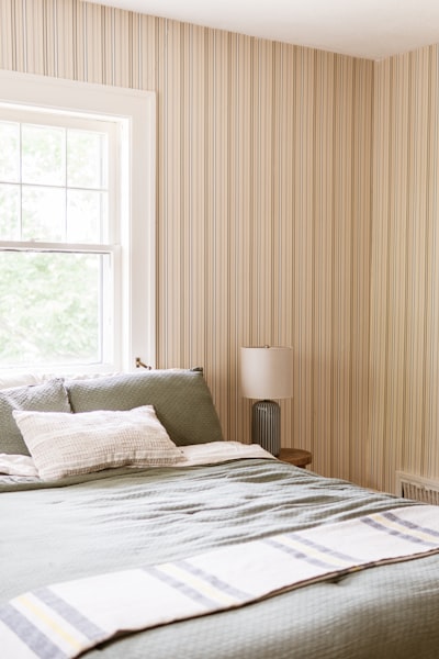 Cozy Bedroom With Green Bedding, Striped Wallpaper, And A Window. wallpaper preview