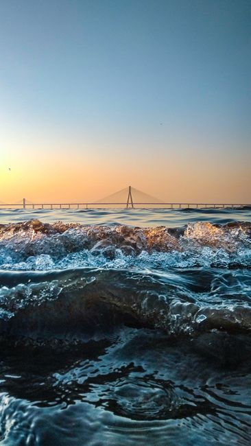 Dramatic Ocean Waves Crashing At Sunset With A Beautiful Bridge In The Distance. wallpaper preview
