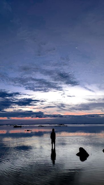 A Serene Silhouette Of A Man Stands By The Ocean At Twilight, Under A Dramatic Cloudy Sky.