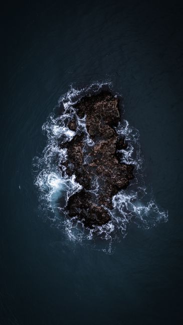 A Dramatic Aerial Shot Captures Waves Crashing Against A Rocky Formation In The Ocean. wallpaper preview