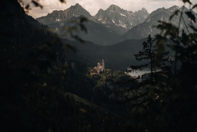 Castle In A Valley Framed By Trees With Mountains Behind. wallpaper preview