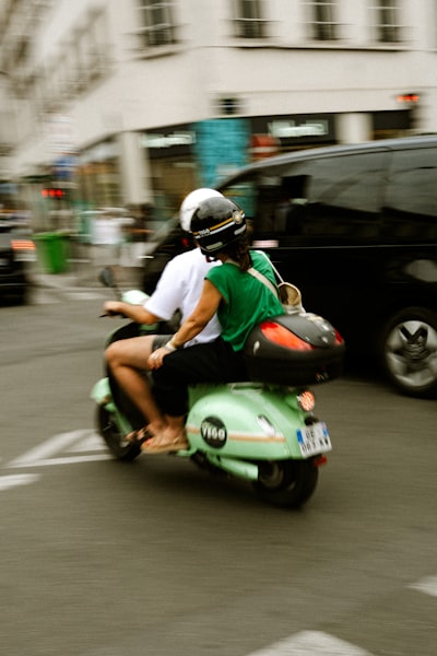 Two People Ride A Green Scooter On A City Street. wallpaper preview