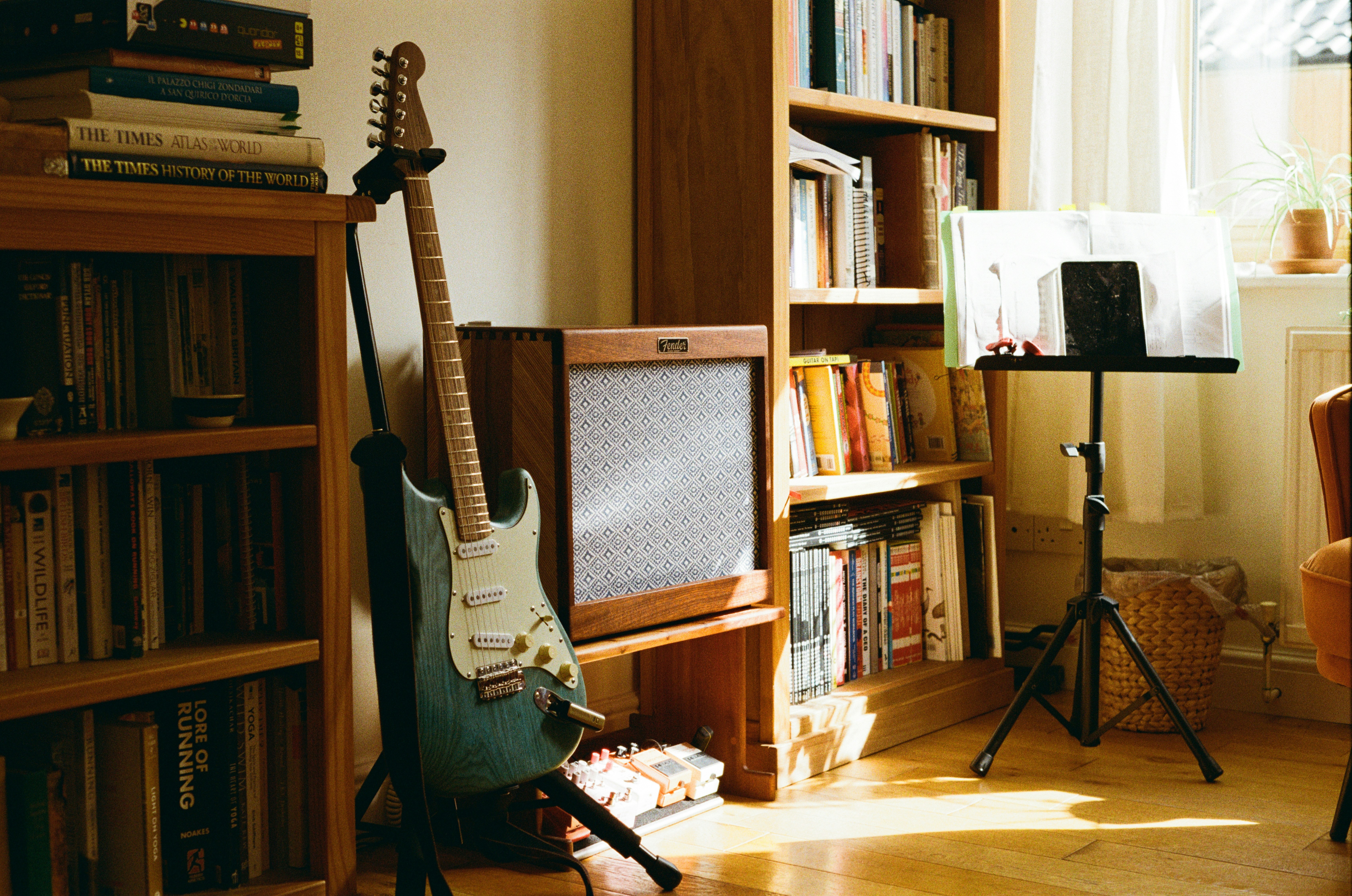 A Blue Electric Guitar Rests Against A Vintage Amp In A Sunlit Room Of Books. HD mobile wallpaper
