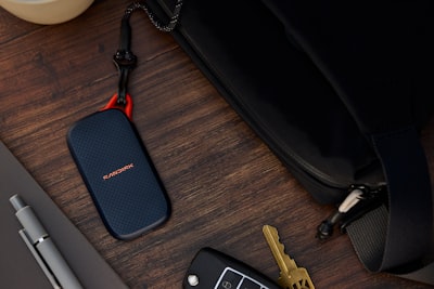 Portable Ssd, Keys, And Pen Next To A Black Bag. wallpaper preview