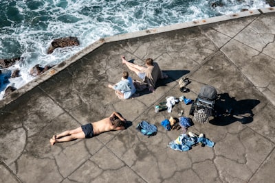 海滩上的宁静人间景色，男人躺卧，两位妇女同坐，周围零散着衣物和婴儿车壁纸预览