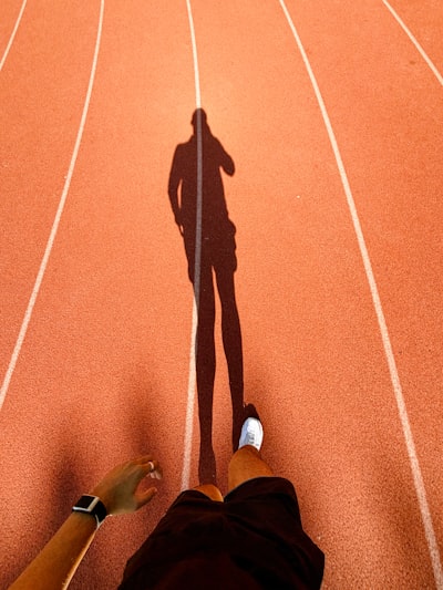 Runner's Shadow Stretching Across An Orange Athletic Track. wallpaper preview