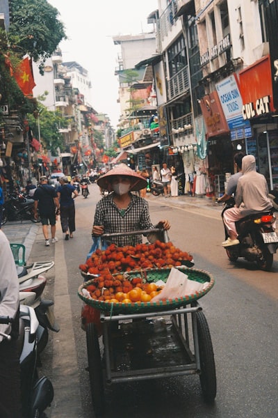 Woman With Conical Hat Pushes Cart Of Fruit On Street wallpaper preview