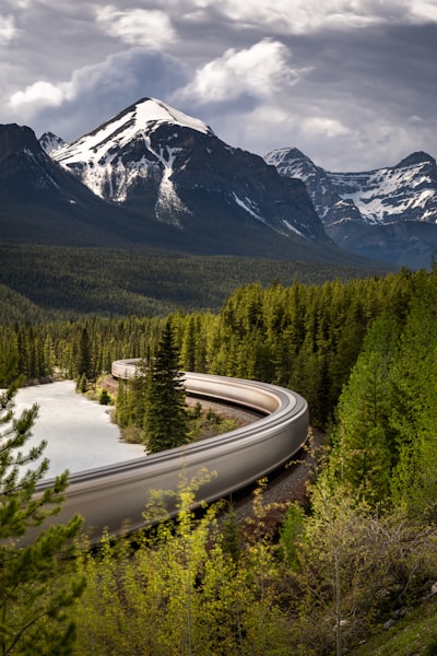A Train Winds Through A Lush Forest With Snow-capped Mountains. wallpaper preview
