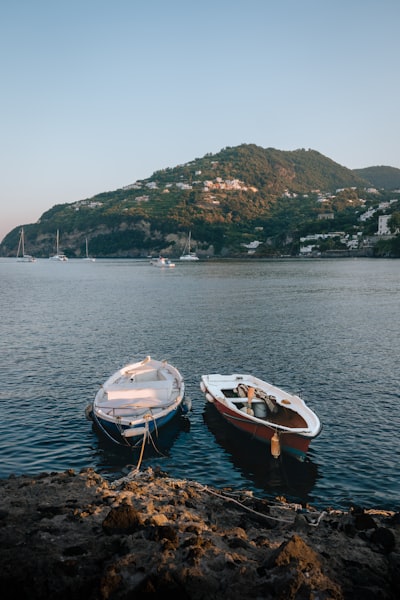 Two Boats Moored By A Rocky Shore, Distant Island. wallpaper preview