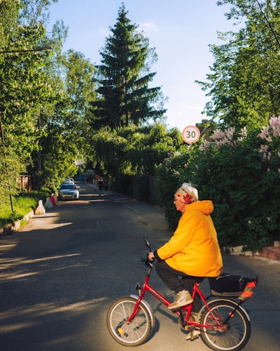 Older Person In Yellow Jacket Rides Red Bicycle On Street. wallpaper preview