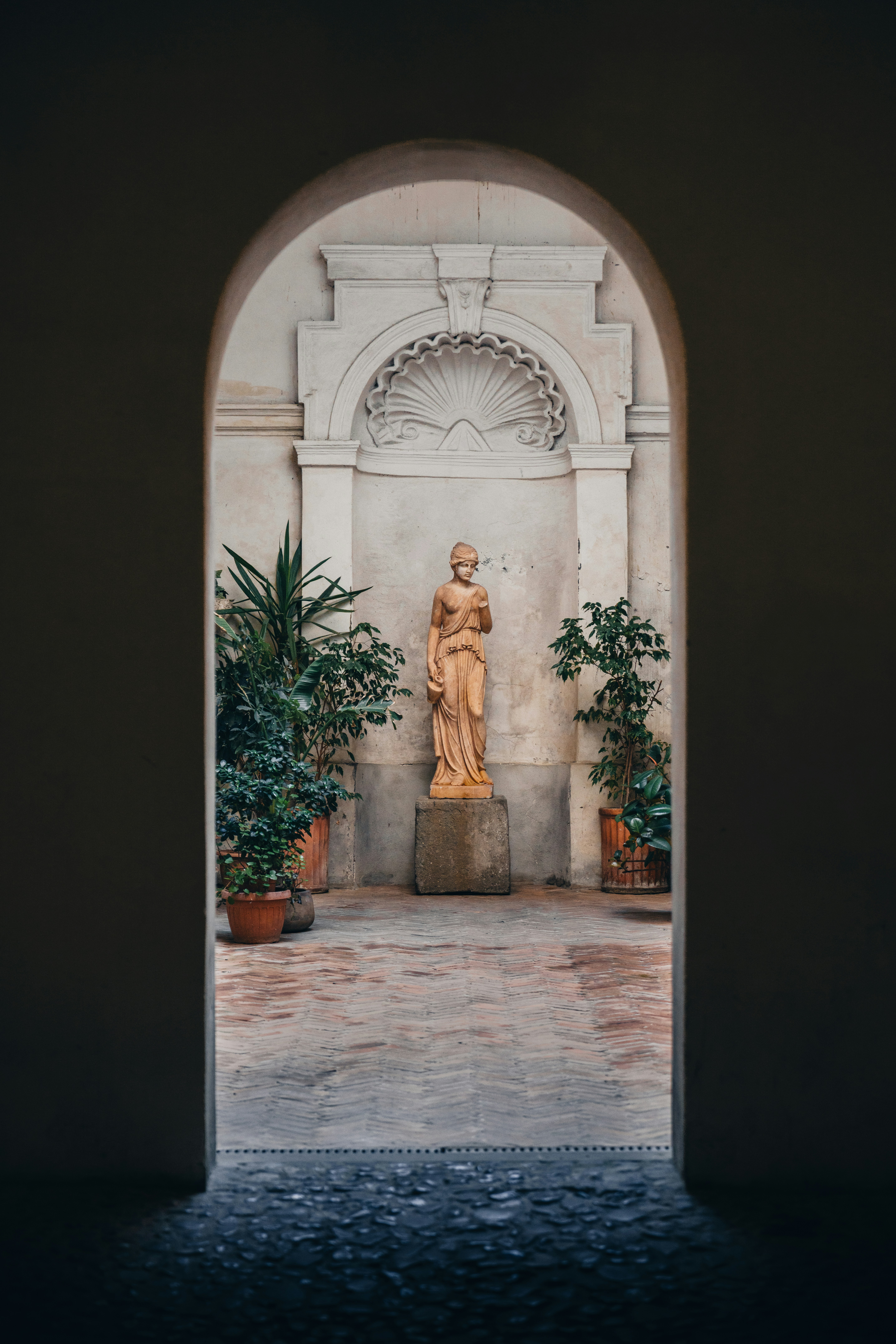 古典-statue静静伫立在庭院中，高耸的拱门将其镶嵌其中，周围的盆栽花卉柔和地环绕手机壁纸高清图片