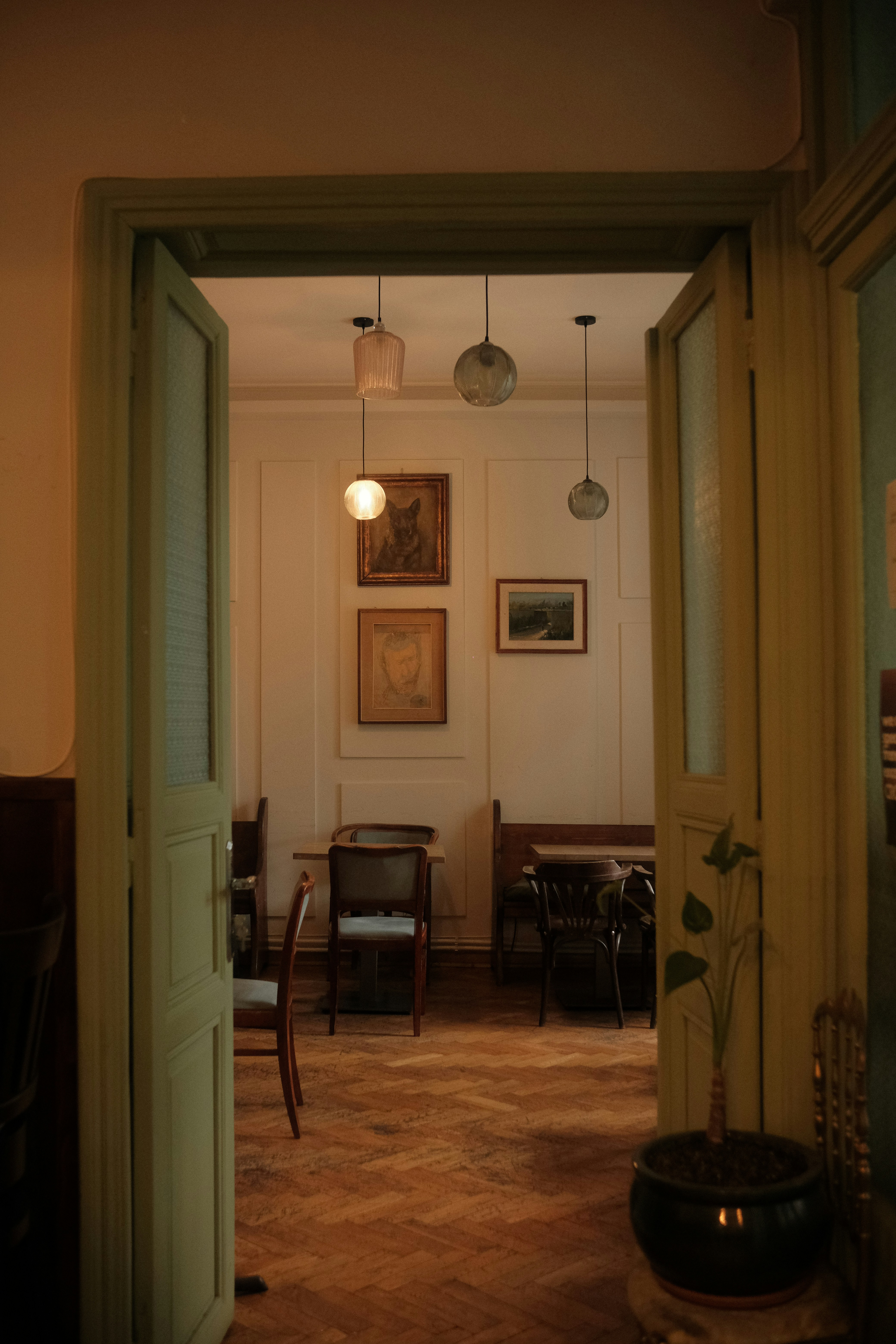 A Softly Lit Vintage Interior Seen Through Open Doors, With Wooden Floors, Hanging Pendant Lights, Framed Artwork, And A Calm Old-world Café Atmosphere. HD mobile wallpaper