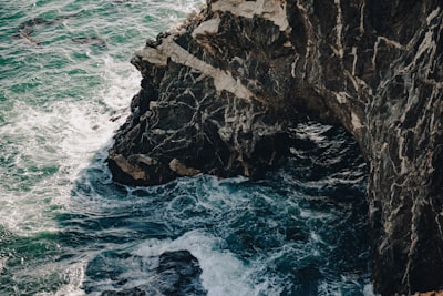 Dark, Rugged Cliffs Meet Foamy, Turbulent Ocean Water. wallpaper preview