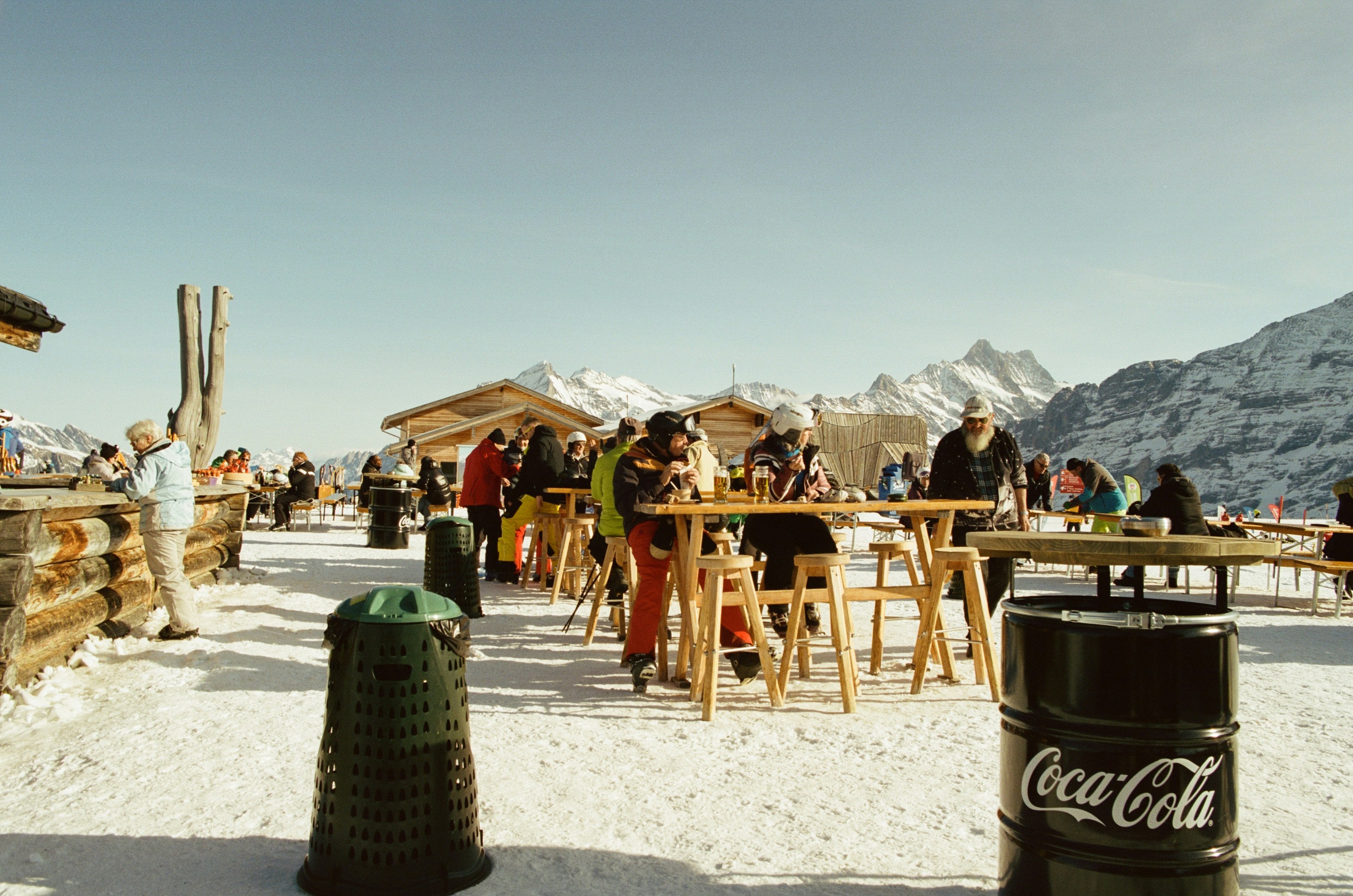 Skiers Gather At A Sunny Mountain Terrace Beneath Sharp Snow-capped Alpine Peaks. HD mobile wallpaper