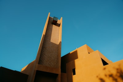 Angular Earth-toned Building With A Prominent Tower Against Blue Sky. wallpaper preview
