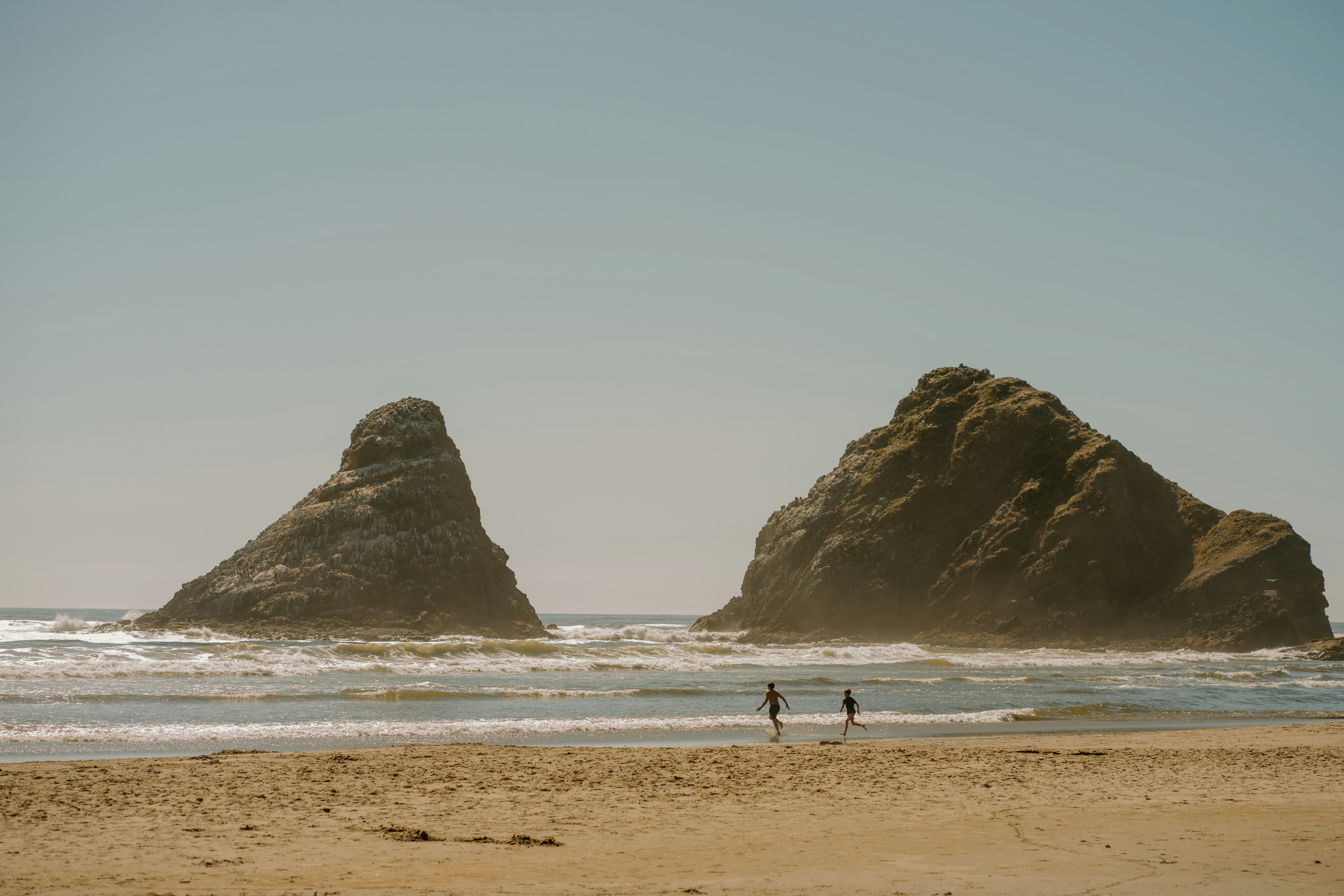 Two People Walking On A Beach Near Large Sea Stacks. HD mobile wallpaper