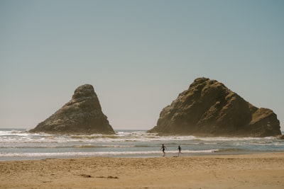 Two People Walking On A Beach Near Large Sea Stacks. wallpaper preview