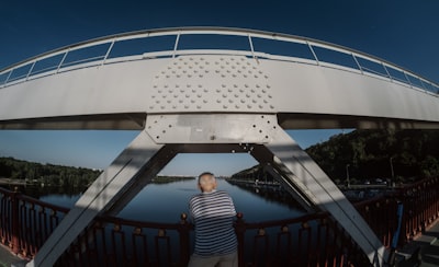Man In Striped Shirt Stands On Bridge Overlooking River. wallpaper preview
