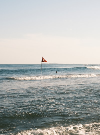 A Red Flag Stands On A Pole In The Ocean. wallpaper preview