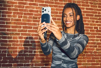 Smiling Woman Takes A Selfie With Smartphone Against Brick Wall. wallpaper preview