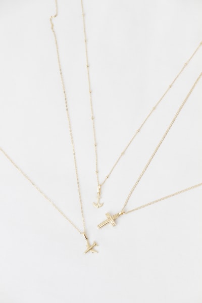 Four Delicate Gold Necklaces With Various Pendants On White Background. wallpaper preview