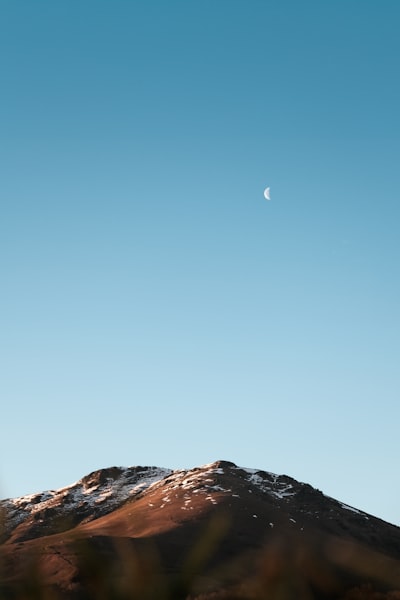 月亮弯在雪山上空的晴蓝天