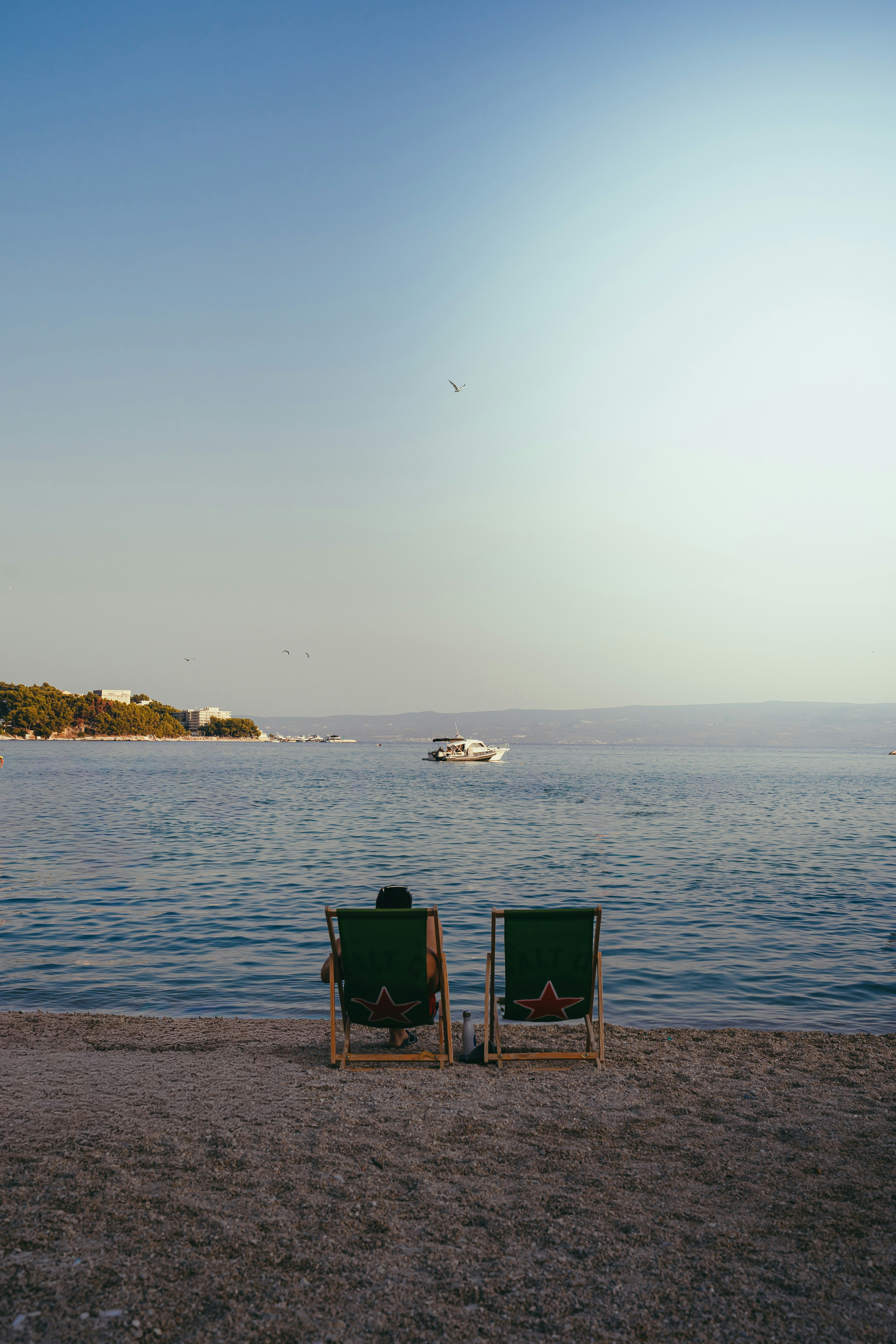 A Person In A Green Deck Chair On A Pebble Beach Facing The Sea HD mobile wallpaper