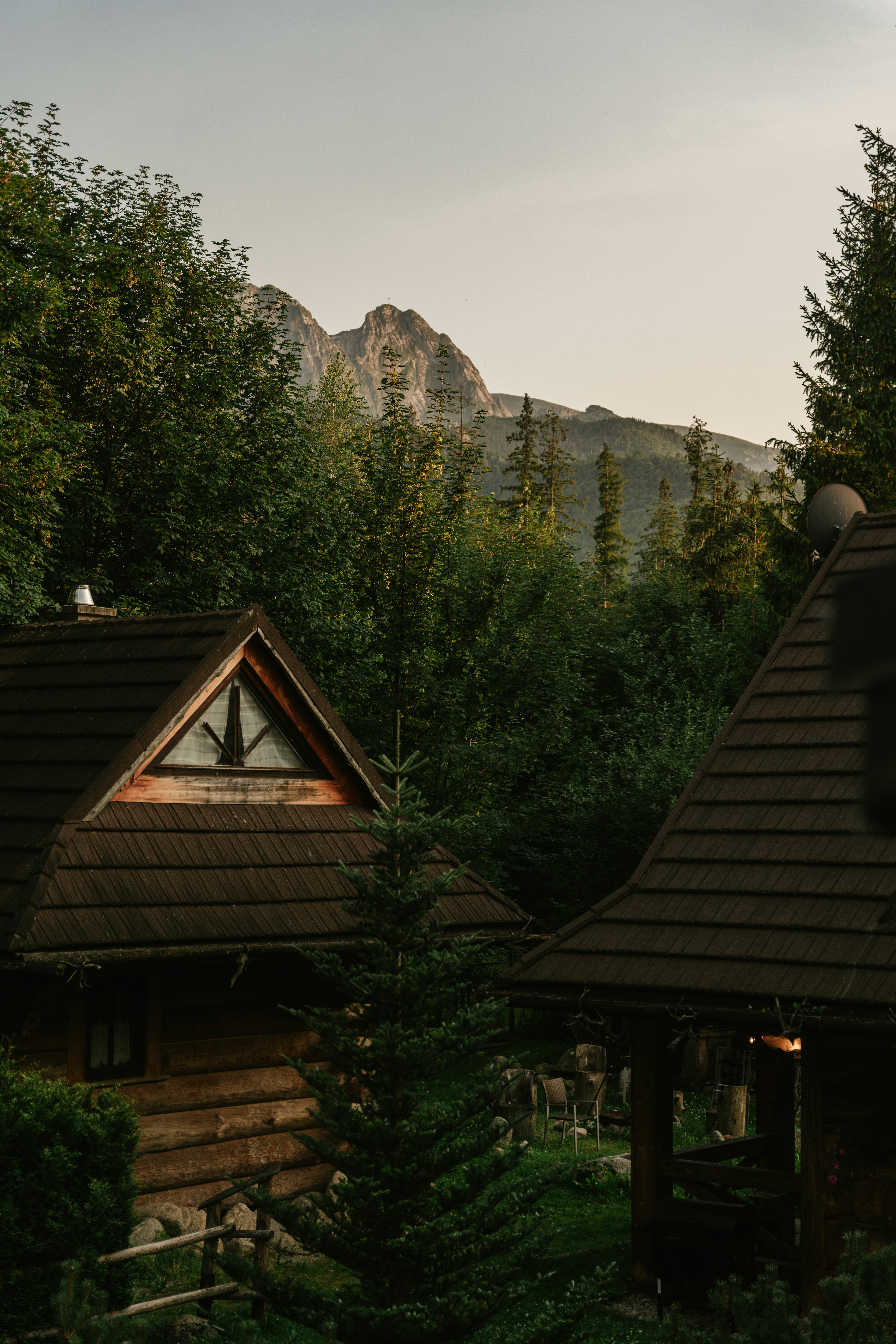 Wooden Cabins With Dark Shingled Roofs Nestled In A Forest Below Rocky Mountain Peaks HD mobile wallpaper