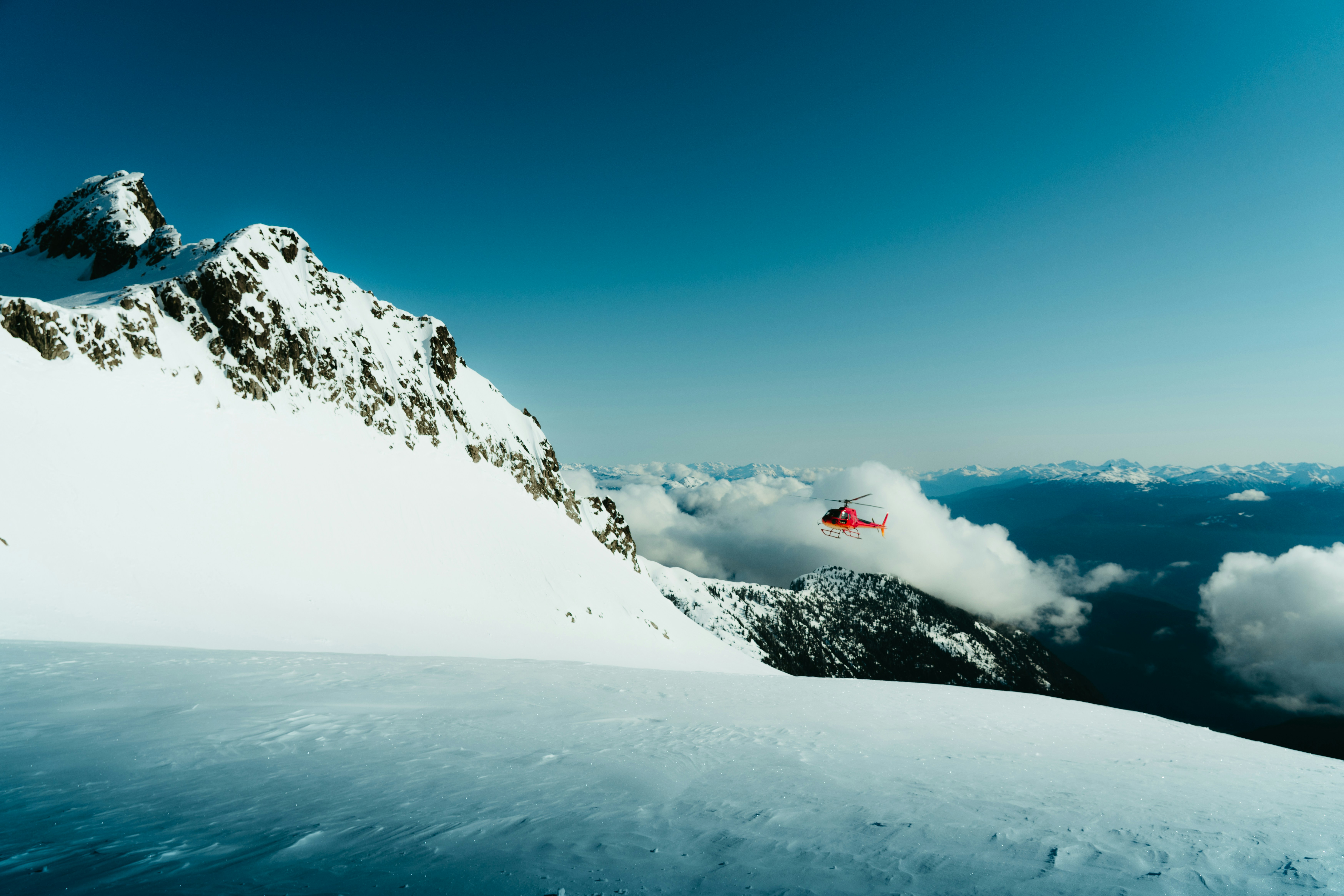 Red Helicopter Flying Near Snow-capped Mountains Under A Blue Sky. HD mobile wallpaper