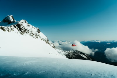 Red Helicopter Flying Near Snow-capped Mountains Under A Blue Sky. wallpaper preview