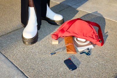 Spilled Red Bag Contents Next To White Boots On Concrete. wallpaper preview