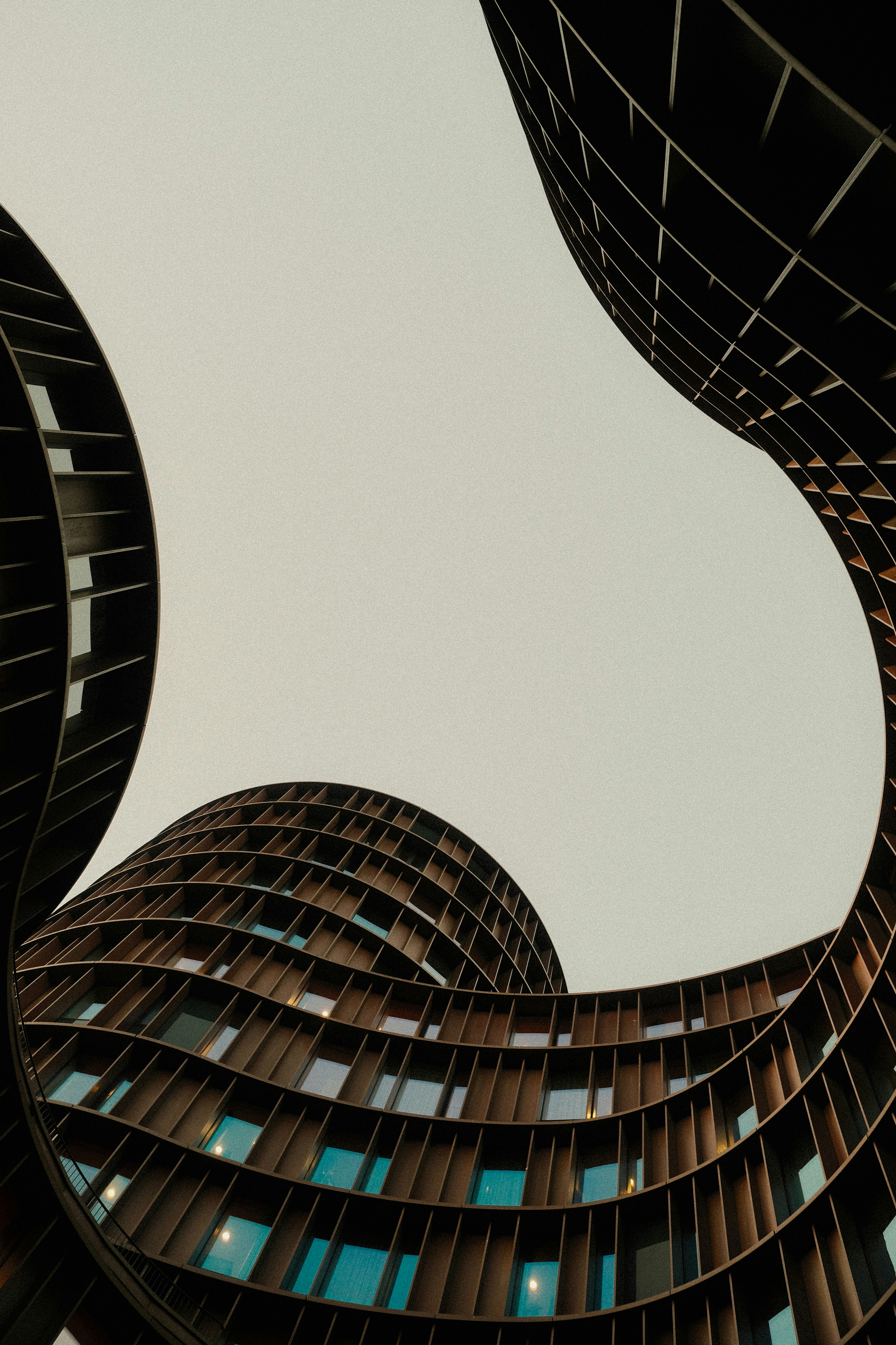 Curved Modern Buildings With Dark Grid Facades Framing A Bright Overcast Sky HD mobile wallpaper