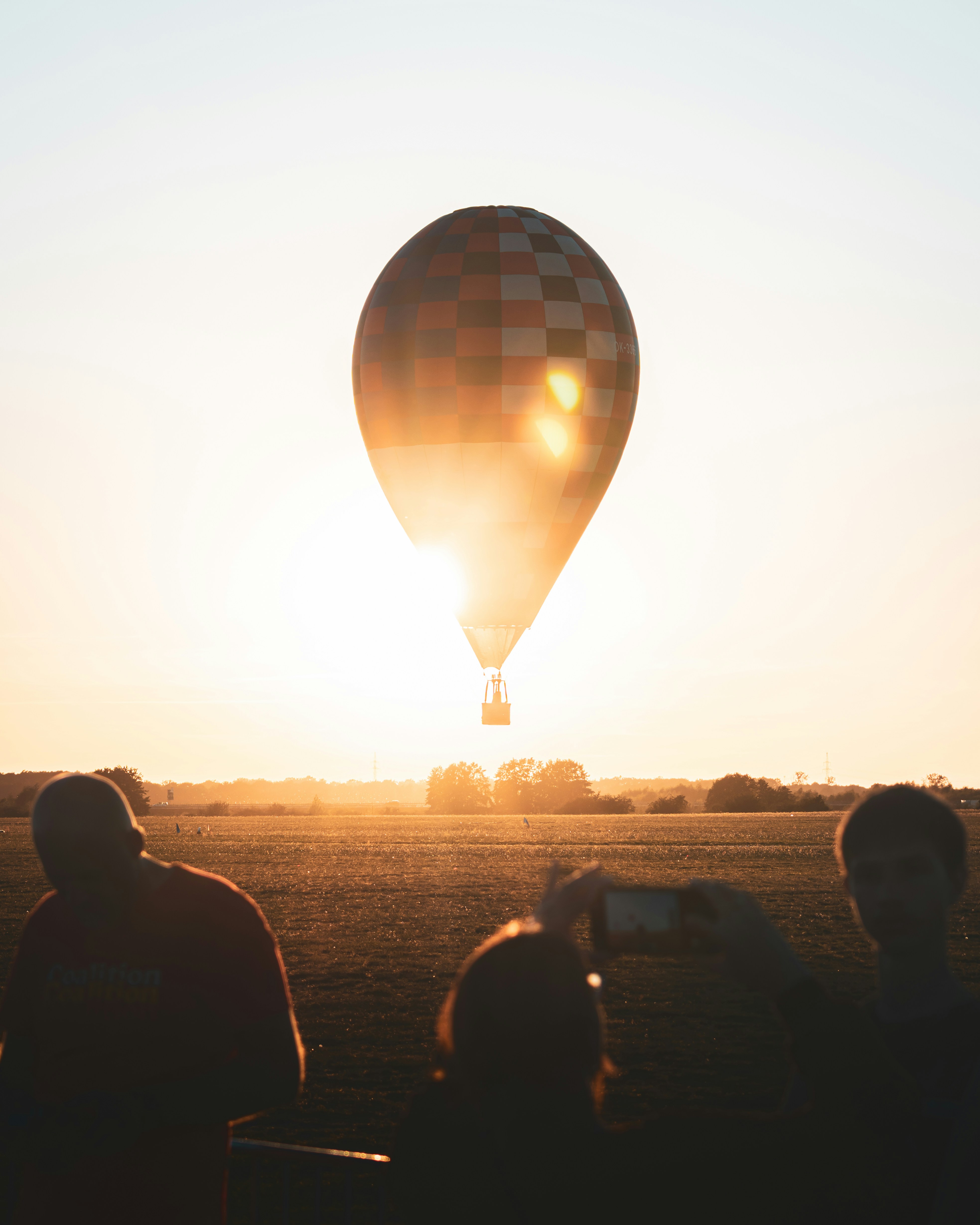 A Checkered Hot Air Balloon Backlit By Low Sun Over A Grassy Field HD mobile wallpaper