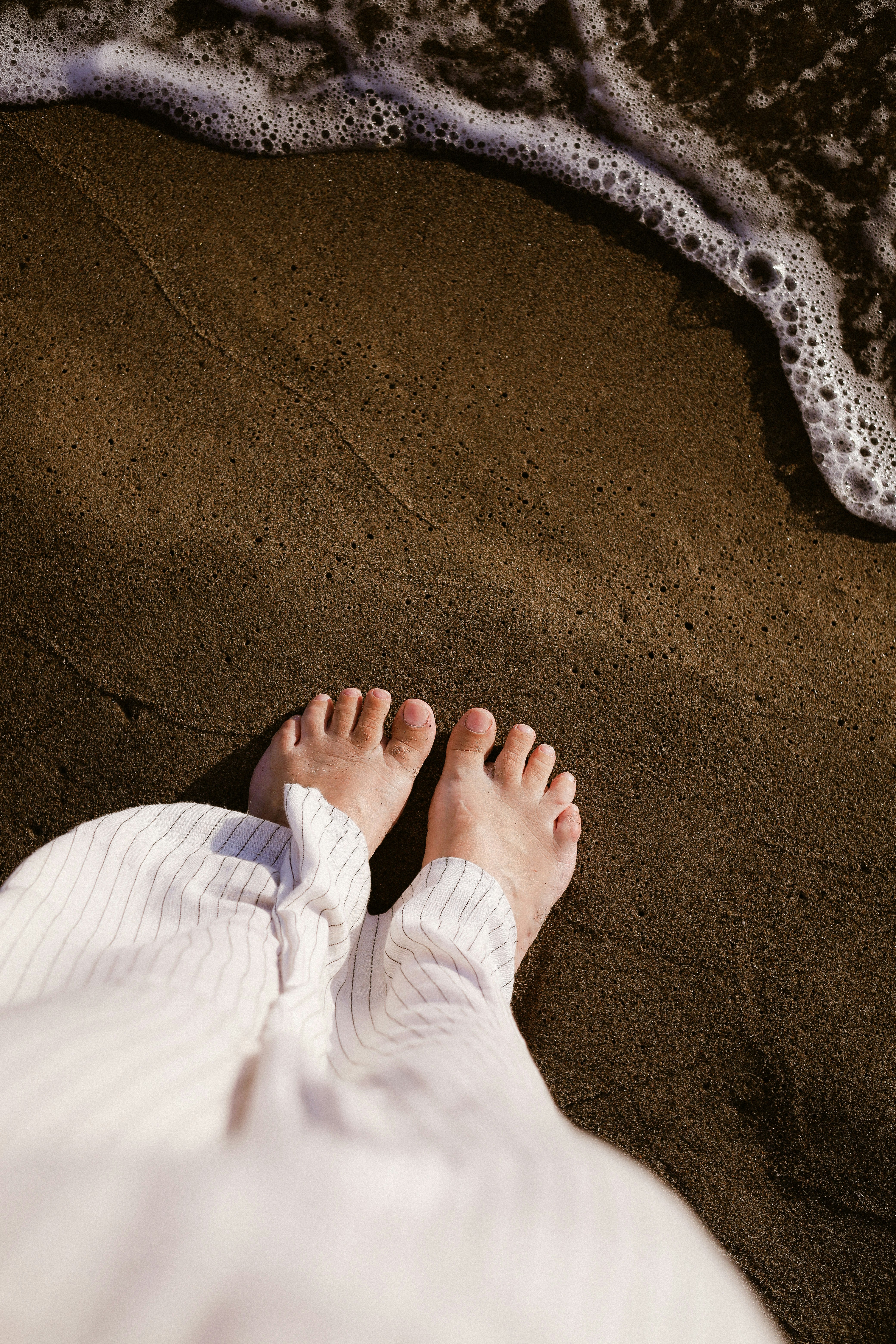 Bare Feet On Wet Dark Sand Near A White Striped Pant Leg HD mobile wallpaper