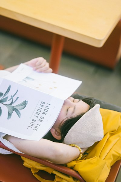 A Person Wearing A Beige Cap Resting With A Magazine Covering Their Face wallpaper preview