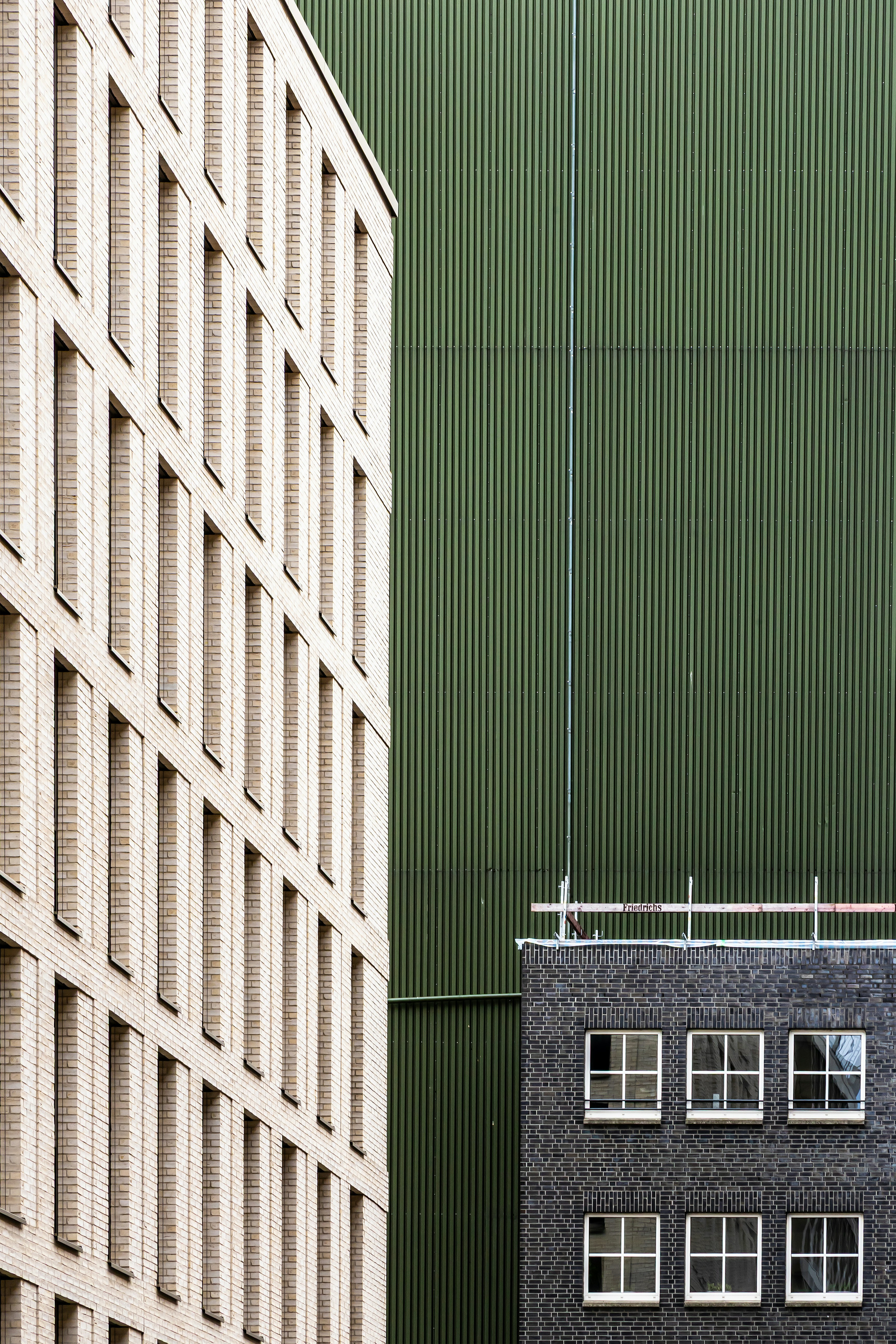 A Beige Brick Building Facade Beside A Green Corrugated Metal Wall And Dark Brick Building HD mobile wallpaper