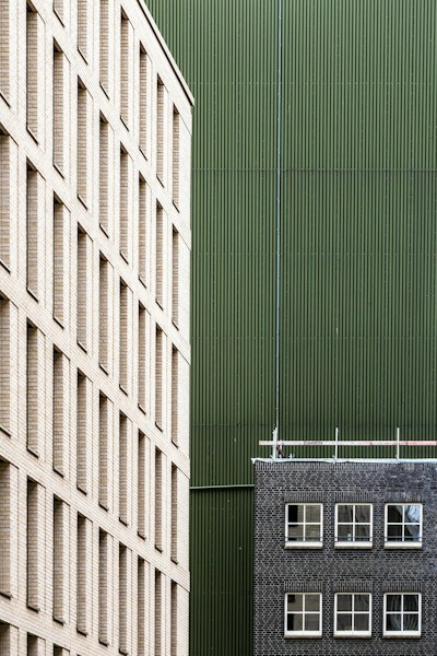 A Beige Brick Building Facade Beside A Green Corrugated Metal Wall And Dark Brick Building wallpaper preview