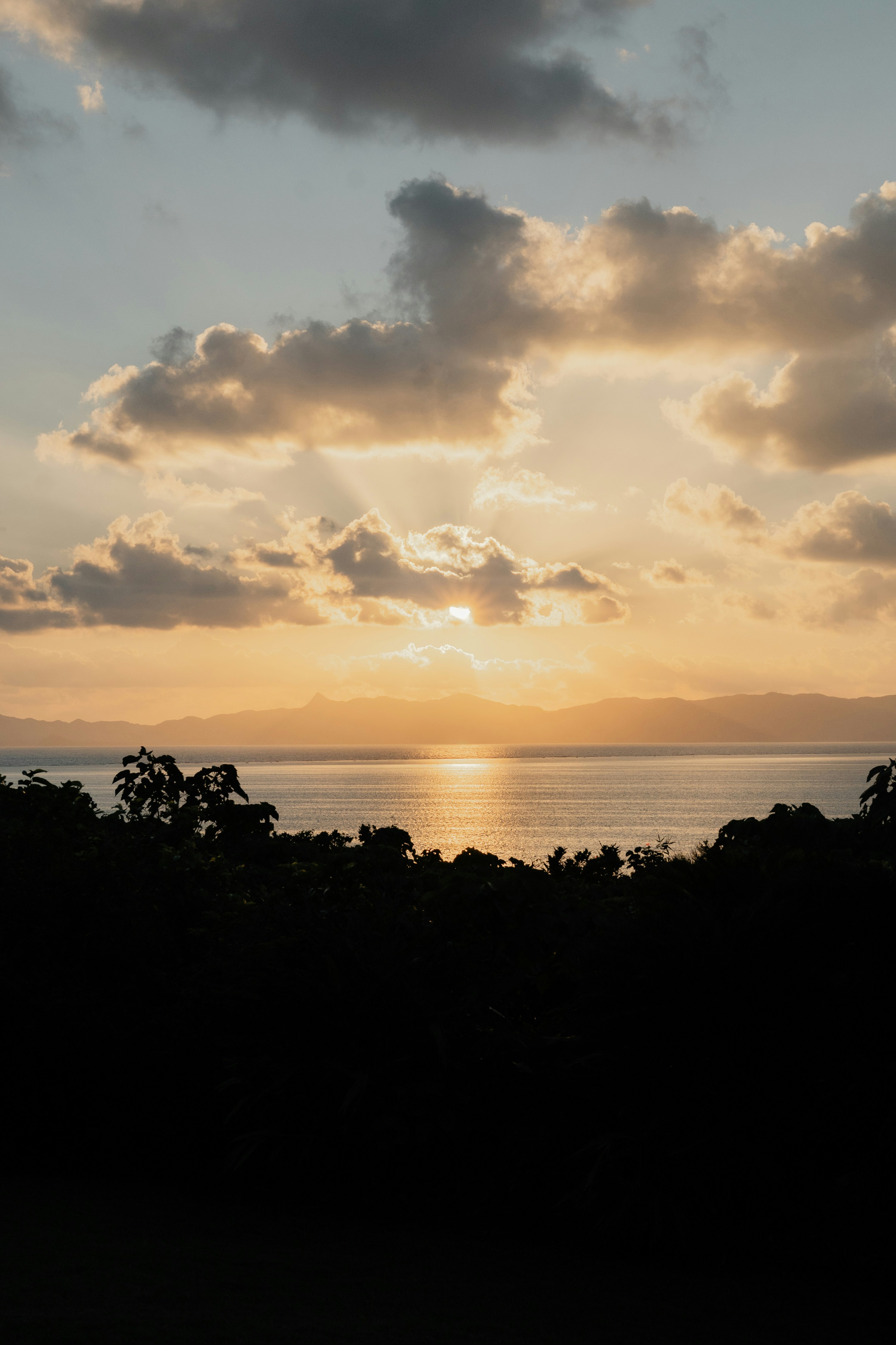 Low Sun Glowing Behind Clouds Over A Calm Sea And Distant Mountain Silhouettes HD mobile wallpaper