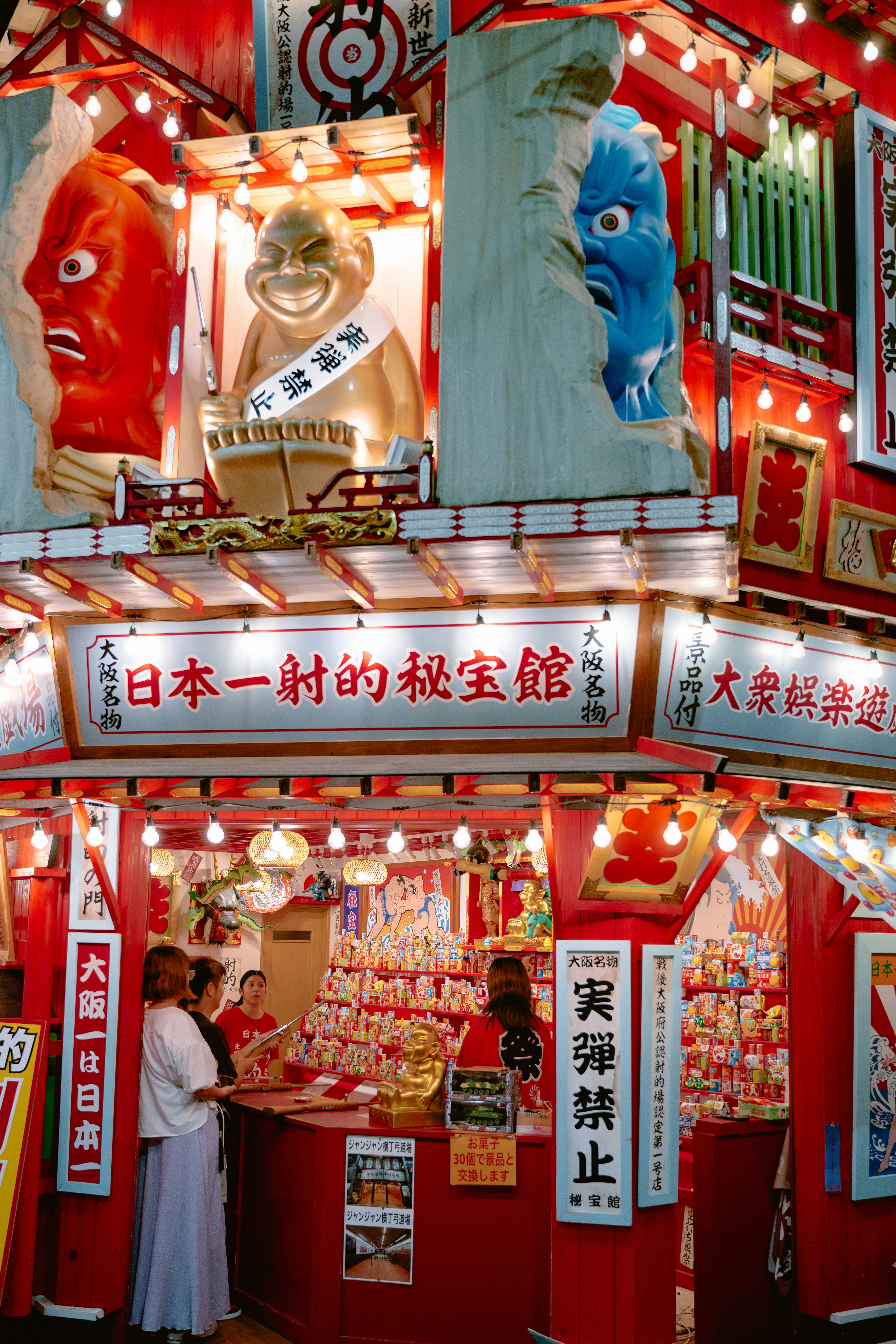 People At A Brightly Lit Red Stall With Colorful Statues In Osaka, Japan HD mobile wallpaper